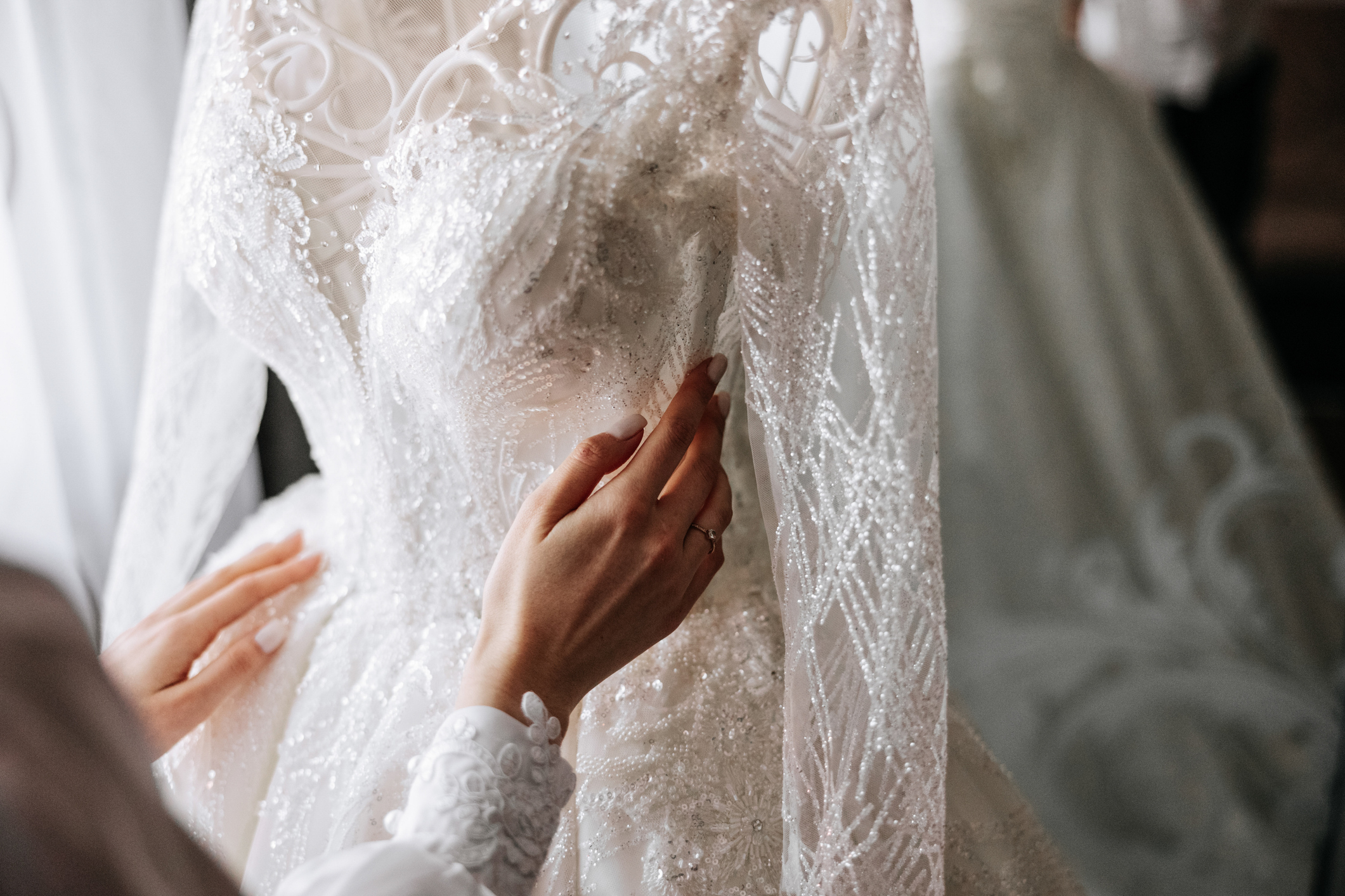 Close-up of a person adjusting the bodice of an ornate white wedding dress decorated with lace and beading.